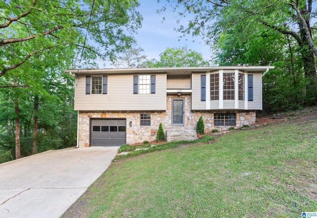 raised ranch with driveway, a front yard, an attached garage, and stone siding