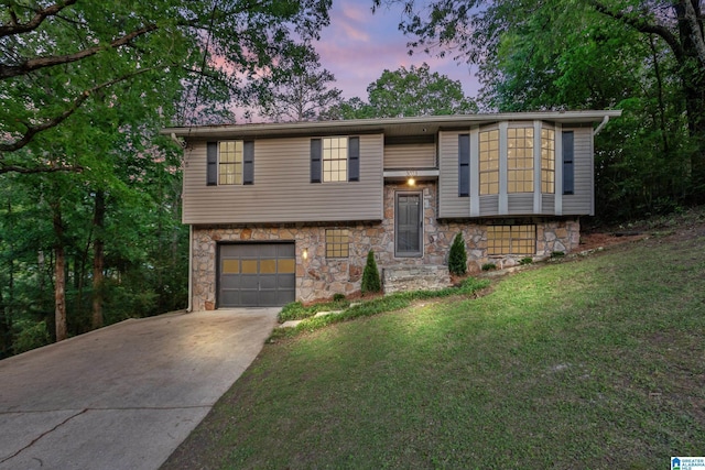 bi-level home featuring a front lawn, driveway, stone siding, and a garage
