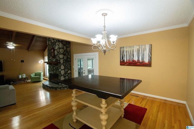 dining room with a stone fireplace, wood finished floors, baseboards, ceiling fan with notable chandelier, and ornamental molding