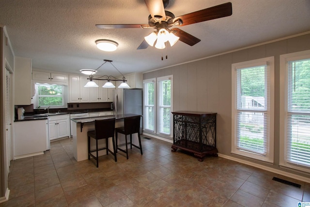 kitchen with a kitchen island, visible vents, dark countertops, white cabinets, and freestanding refrigerator