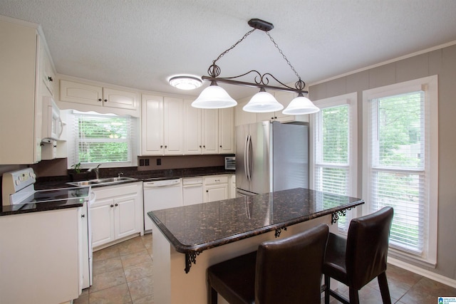 kitchen featuring hanging light fixtures, a sink, white appliances, a breakfast bar area, and white cabinetry