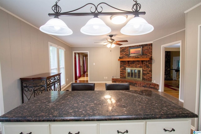 kitchen with a ceiling fan, crown molding, a brick fireplace, white cabinets, and open floor plan
