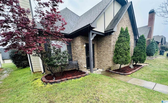 view of side of property featuring a lawn, roof with shingles, and brick siding