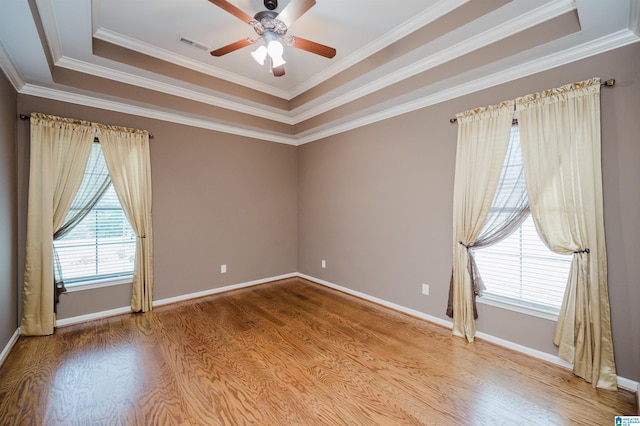 spare room with ceiling fan, baseboards, wood finished floors, a tray ceiling, and visible vents