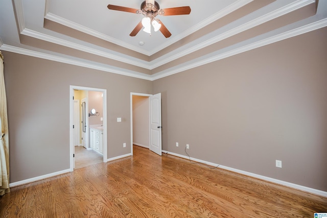 unfurnished bedroom featuring light wood-style floors, ornamental molding, a raised ceiling, and ensuite bathroom