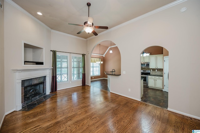 unfurnished living room with ceiling fan, a tiled fireplace, arched walkways, ornamental molding, and dark wood-type flooring