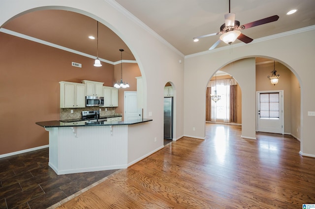 kitchen with visible vents, a breakfast bar, ceiling fan with notable chandelier, backsplash, and stainless steel appliances
