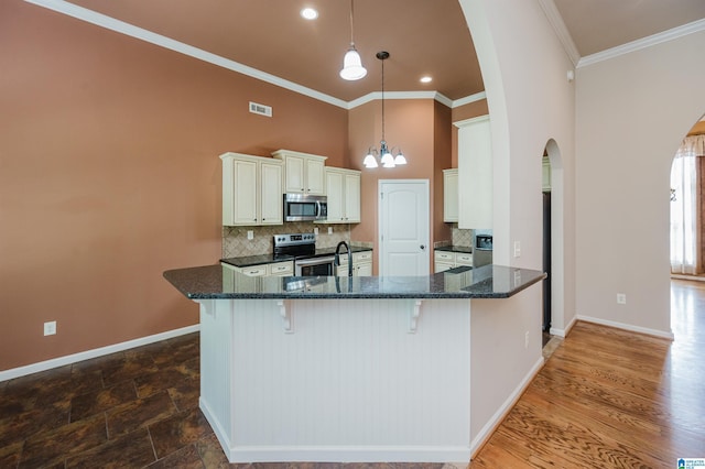 kitchen featuring decorative backsplash, crown molding, appliances with stainless steel finishes, arched walkways, and baseboards