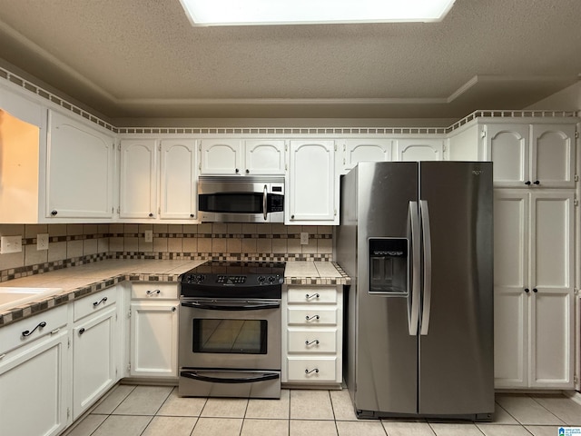 kitchen featuring light tile patterned floors, appliances with stainless steel finishes, tile counters, and a textured ceiling