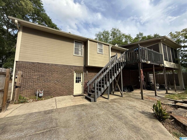 rear view of house featuring brick siding, a wooden deck, stairs, and a patio area