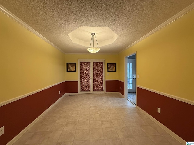 spare room with baseboards, ornamental molding, a textured ceiling, and a tray ceiling