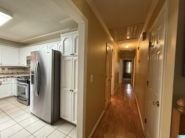 hallway featuring ornamental molding, baseboards, attic access, a textured ceiling, and light tile patterned floors