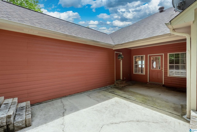 property entrance featuring a shingled roof and a patio area