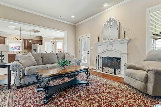living area featuring recessed lighting, a fireplace with raised hearth, visible vents, ornamental molding, and wood finished floors