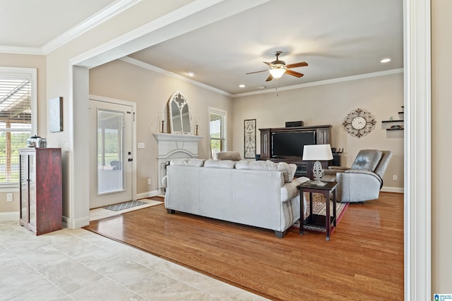 living area featuring crown molding, ceiling fan, baseboards, and a healthy amount of sunlight
