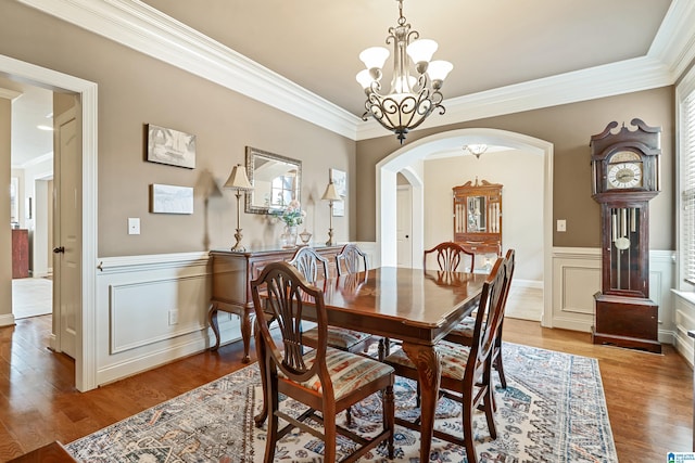 dining space featuring wood finished floors, a wainscoted wall, ornamental molding, and arched walkways