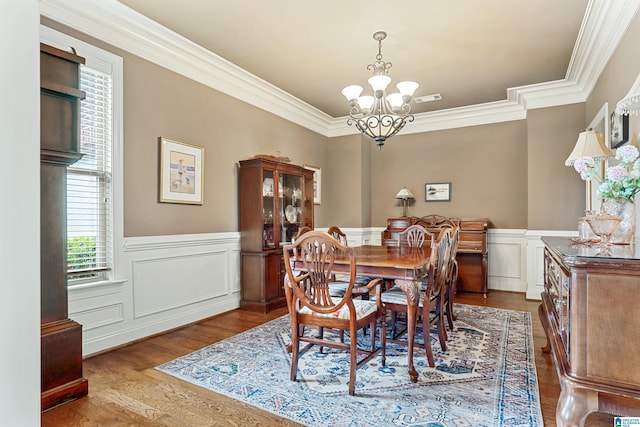 dining space featuring wood finished floors, a chandelier, wainscoting, ornamental molding, and visible vents