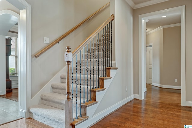 staircase with crown molding, arched walkways, wood finished floors, and baseboards