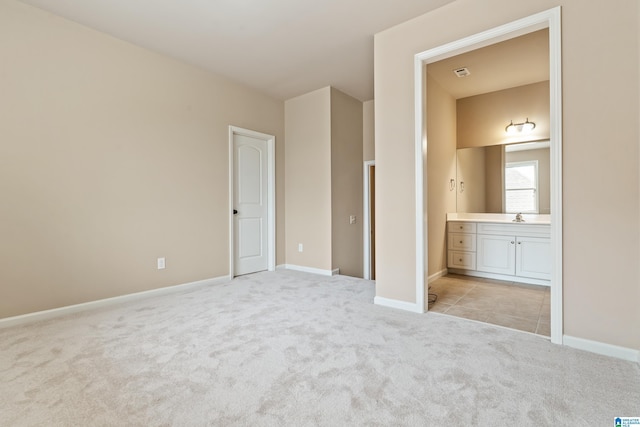 unfurnished bedroom with connected bathroom, a sink, light colored carpet, and baseboards