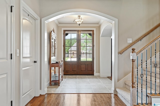 foyer entrance with crown molding, light wood-style flooring, baseboards, arched walkways, and stairs