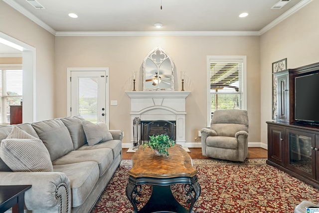 living area featuring a fireplace with raised hearth, ceiling fan, visible vents, ornamental molding, and wood finished floors