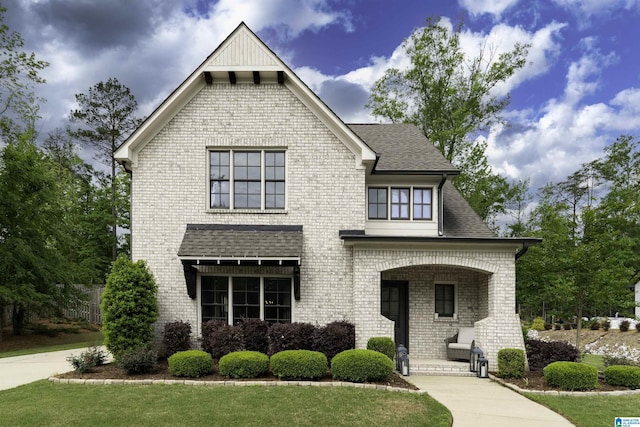 view of front of house featuring a porch, a shingled roof, and brick siding