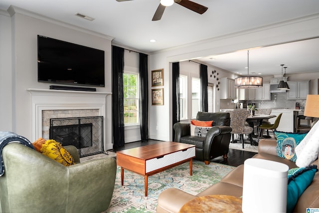 living area with recessed lighting, wood finished floors, ornamental molding, ceiling fan with notable chandelier, and a fireplace