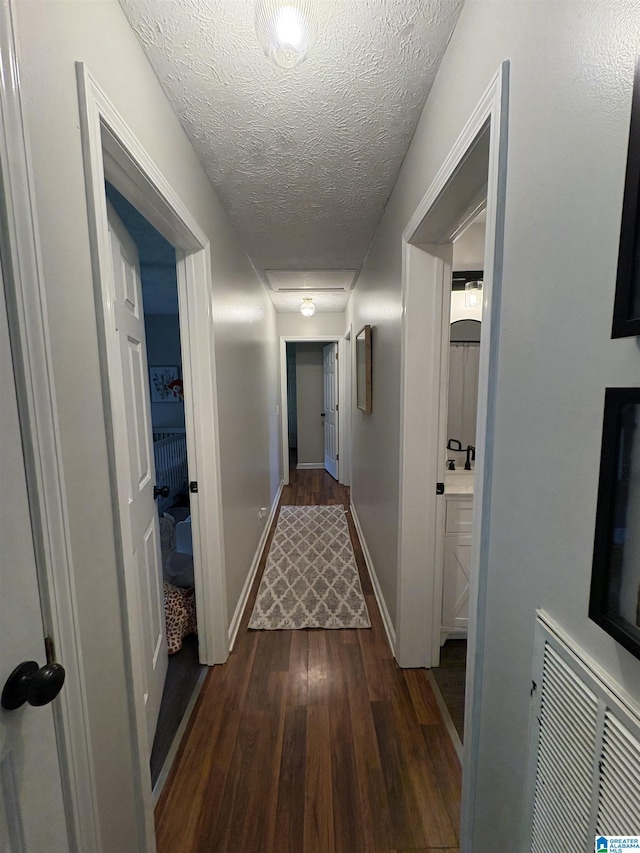 hallway featuring a textured ceiling, visible vents, dark wood-style floors, and baseboards