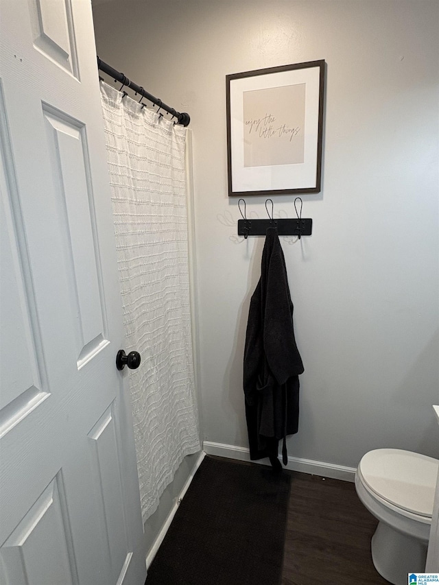 bathroom featuring baseboards, wood finished floors, and toilet