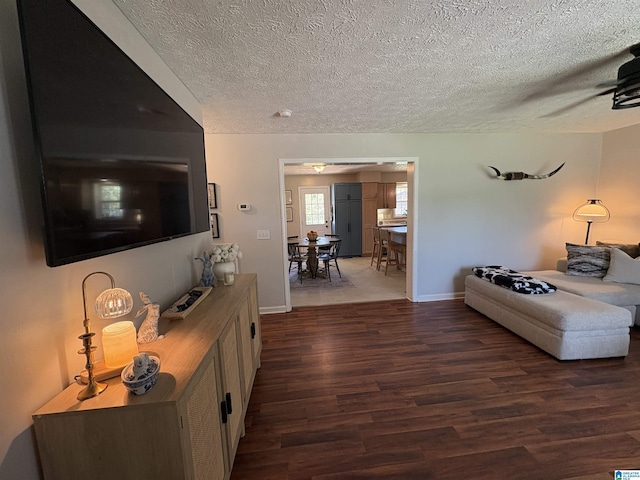 living room with a textured ceiling, a ceiling fan, dark wood finished floors, and baseboards