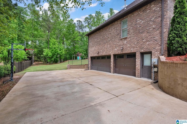 view of property exterior featuring concrete driveway, a playground, a yard, brick siding, and a garage