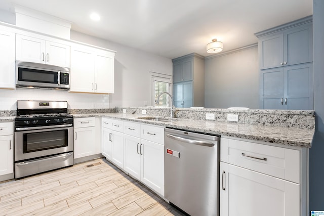 2607 Woodfern Ct, Homewood, AL 35209 - kitchen featuring appliances with stainless steel finishes, light stone counters, a sink, a peninsula, and light wood-type flooring
