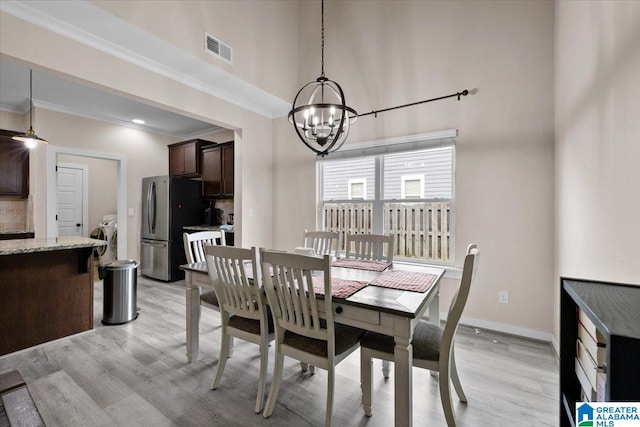 dining space with a high ceiling, an inviting chandelier, visible vents, and light wood-style floors