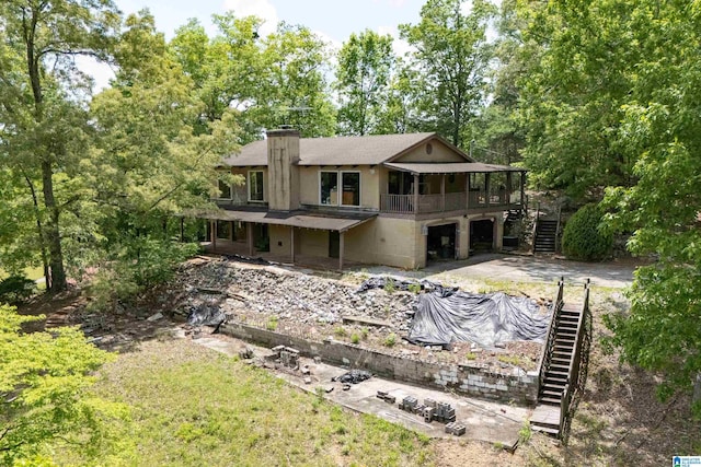 rear view of property featuring stairway, driveway, a chimney, and a garage