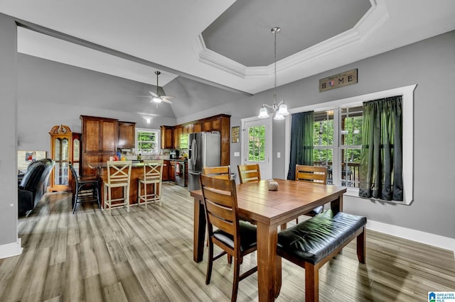 dining area with crown molding, light wood-type flooring, a raised ceiling, and baseboards