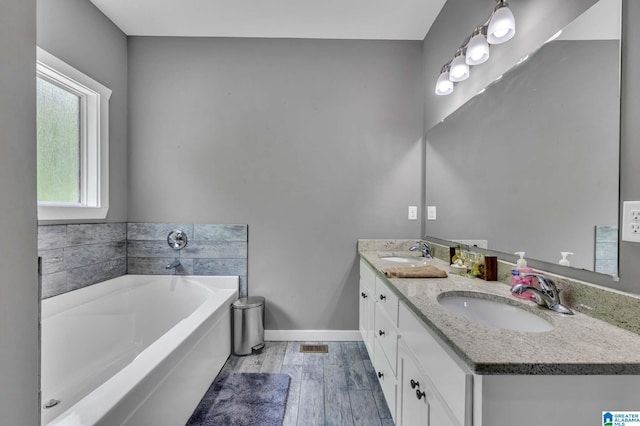 full bath featuring a garden tub, double vanity, a sink, and baseboards