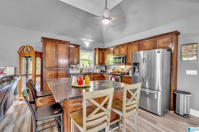 kitchen featuring stainless steel appliances, ceiling fan, brown cabinetry, light wood-type flooring, and vaulted ceiling