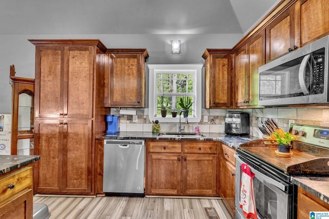 kitchen featuring light wood-type flooring, backsplash, appliances with stainless steel finishes, and a sink
