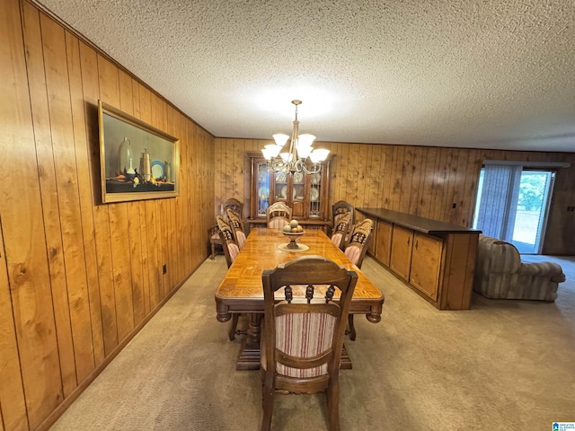 dining room with light colored carpet, wood walls, a chandelier, and a textured ceiling