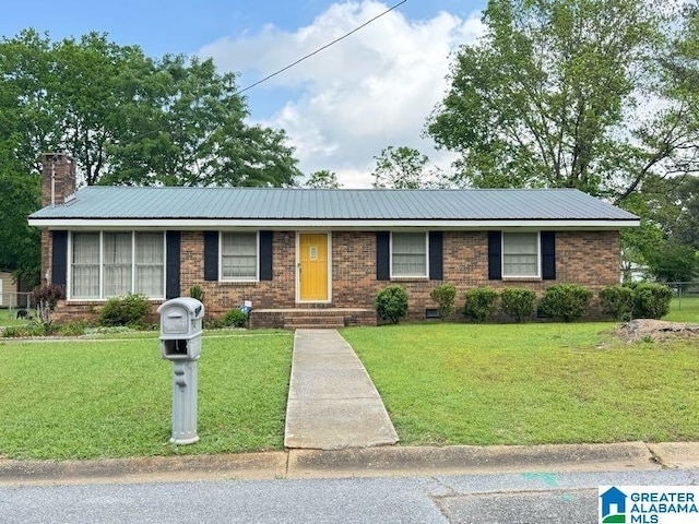 ranch-style home with a chimney, brick siding, a front yard, and metal roof