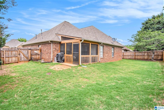 rear view of house with brick siding, a sunroom, a fenced backyard, a gate, and a yard