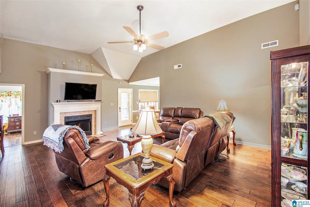 living room with a ceiling fan, visible vents, a tiled fireplace, vaulted ceiling, and dark wood-style floors
