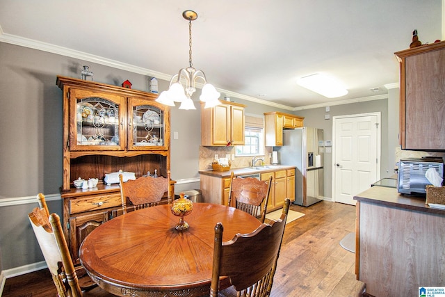 dining area with an inviting chandelier, light wood-style flooring, baseboards, a toaster, and ornamental molding