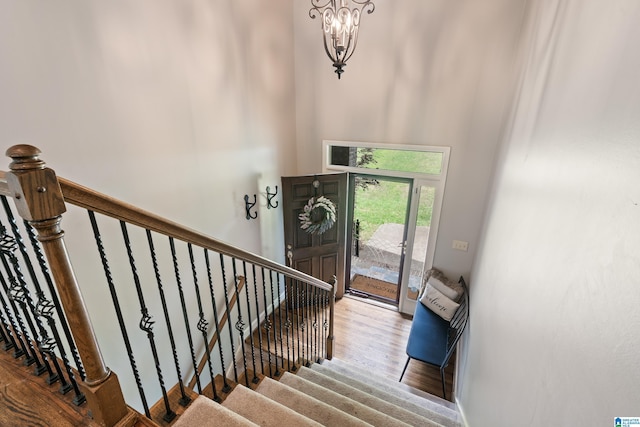 stairs with a towering ceiling, wood finished floors, and a chandelier