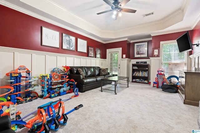 carpeted living room featuring a decorative wall, ceiling fan, healthy amount of natural light, crown molding, and wainscoting