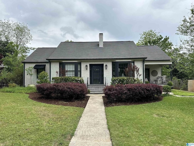 view of front of property featuring brick siding, a front lawn, fence, and a chimney