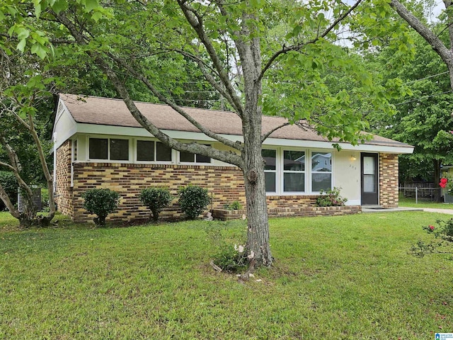 ranch-style home with a front yard, a shingled roof, and brick siding