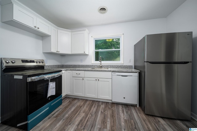kitchen with light stone countertops, stainless steel appliances, white cabinets, a sink, and dark wood-type flooring