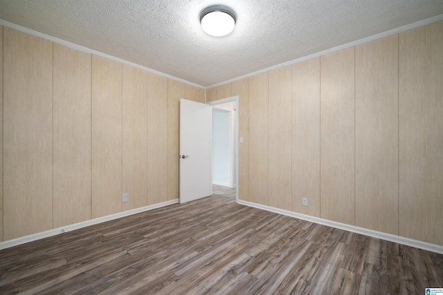 empty room with a textured ceiling, wood finished floors, ornamental molding, and baseboards