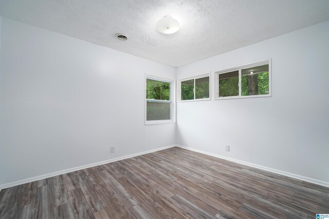 spare room with baseboards, visible vents, wood finished floors, and a textured ceiling
